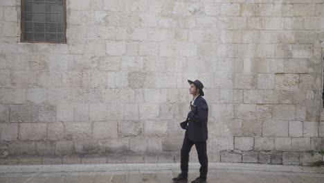 orthodox jewish male walks past old wall with book in the old city, jerusalem