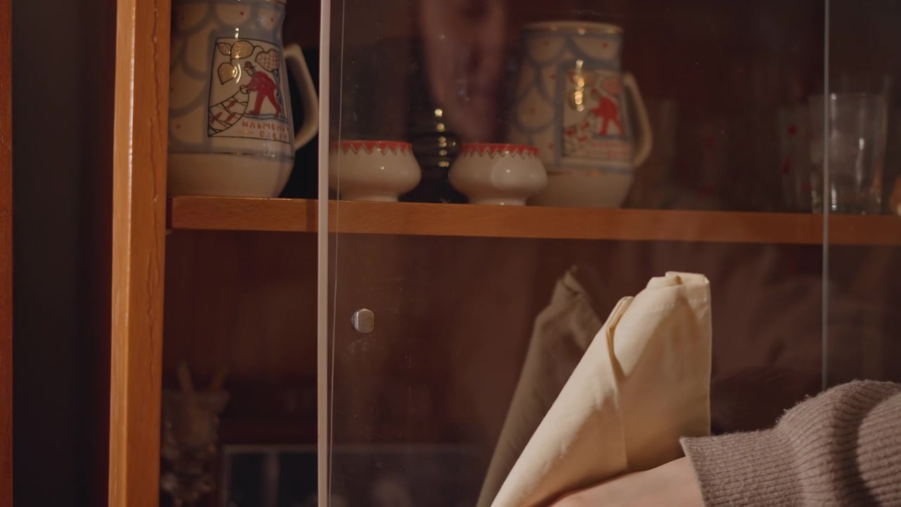 Caucasian woman polishing porcelain teapot. Intimate cabinet scene with careful hands arranging ceramics, curator mindset, warm wood shelves, gentle buffing motion, preserved collection, quiet focus