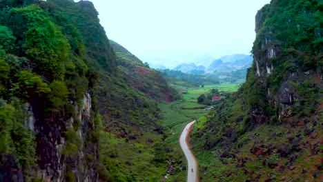 Eine-Stark-Befahrene-Straße-Mit-Motorrädern-Durchschneidet-Zwei-Berge-Und-Enthüllt-üppiges-Ackerland-Inmitten-Der-Nebligen-Kulisse-Im-Norden-Vietnams