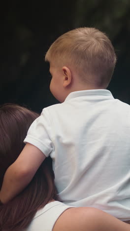 madre y hijo felices admiran la cascada con agua clara de primer plano vista trasera. la mujer sostiene al niño en los brazos y el niño abraza al cuello de la madre con ternura en cámara lenta