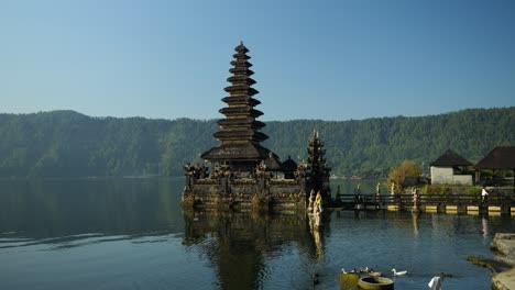 Zeitlupenschwenkaufnahme-Des-Pura-Ulun-Danu-Tempels-Mit-Blick-Auf-Den-Vulkansee-Und-Die-Umliegende-Natur-Mit-Schwimmenden-Enten