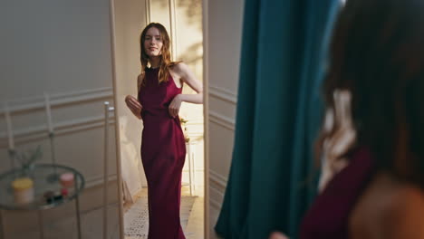 woman reflection trying dress in sunny room. smiling girl admiring red outfit