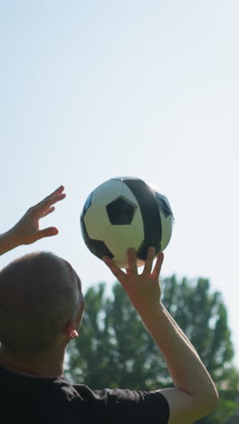 primer plano de un hombre de mediana edad hábilmente girando una pelota de fútbol en el aire con árboles en el fondo y un cielo azul claro
