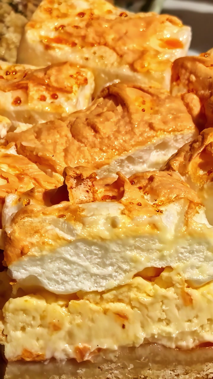 Primo piano di un dessert meringato dorato con strati di ripieno cremoso, accompagnato da carne in crosta di erbe. Ideale per blog culinari o programmi di cucina.