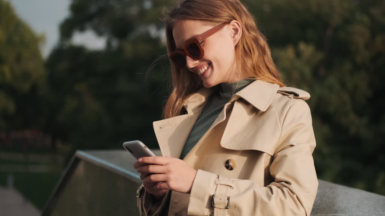 Caucasian female student using smartphone and smiling outdoors.