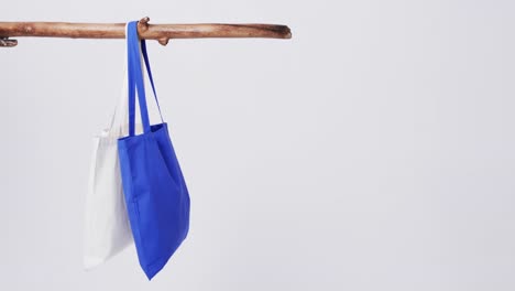 Video-of-blue-and-white-canvas-bags-hanging-from-branch-with-copy-space-on-white-background