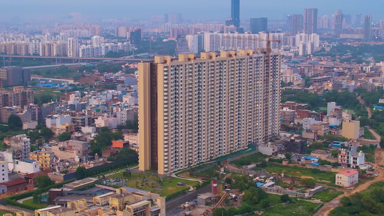 Imagem de drone aéreo descendo perto de um edifício em construção com guindaste no topo, com a paisagem urbana de Delhi ao longe, mostrando o desenvolvimento em Noida, Chennai, Mumbai.