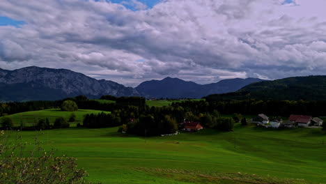 Aerial-drone-forward-moving-shot-over-green-grasslands-at-the-foothills-of-a-mountain-range-on-a-cloudy-day