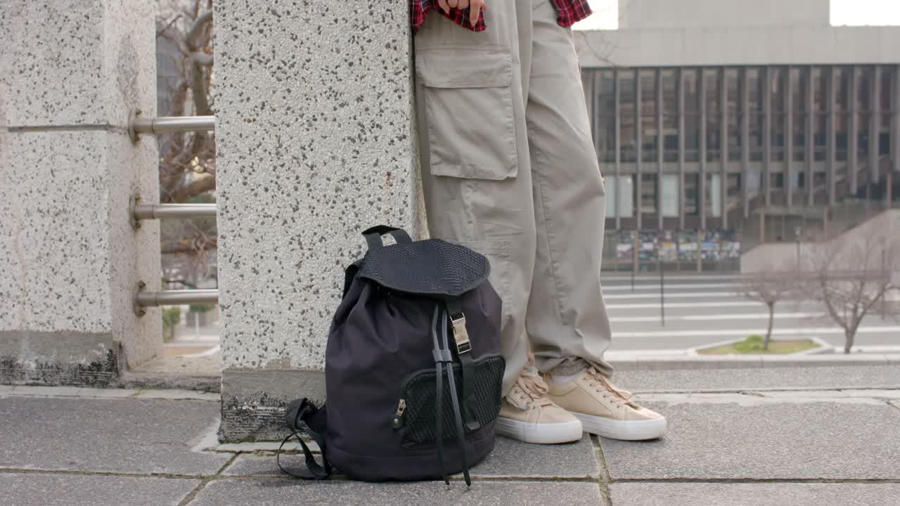 Upon lowering backpack person is lifting right foot and bracing sneaker against pillar balancing