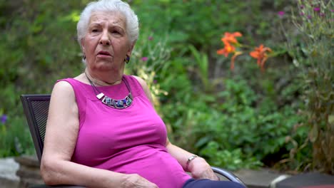 elderly woman has a face of amazement and shock while sitting outside in a garden area