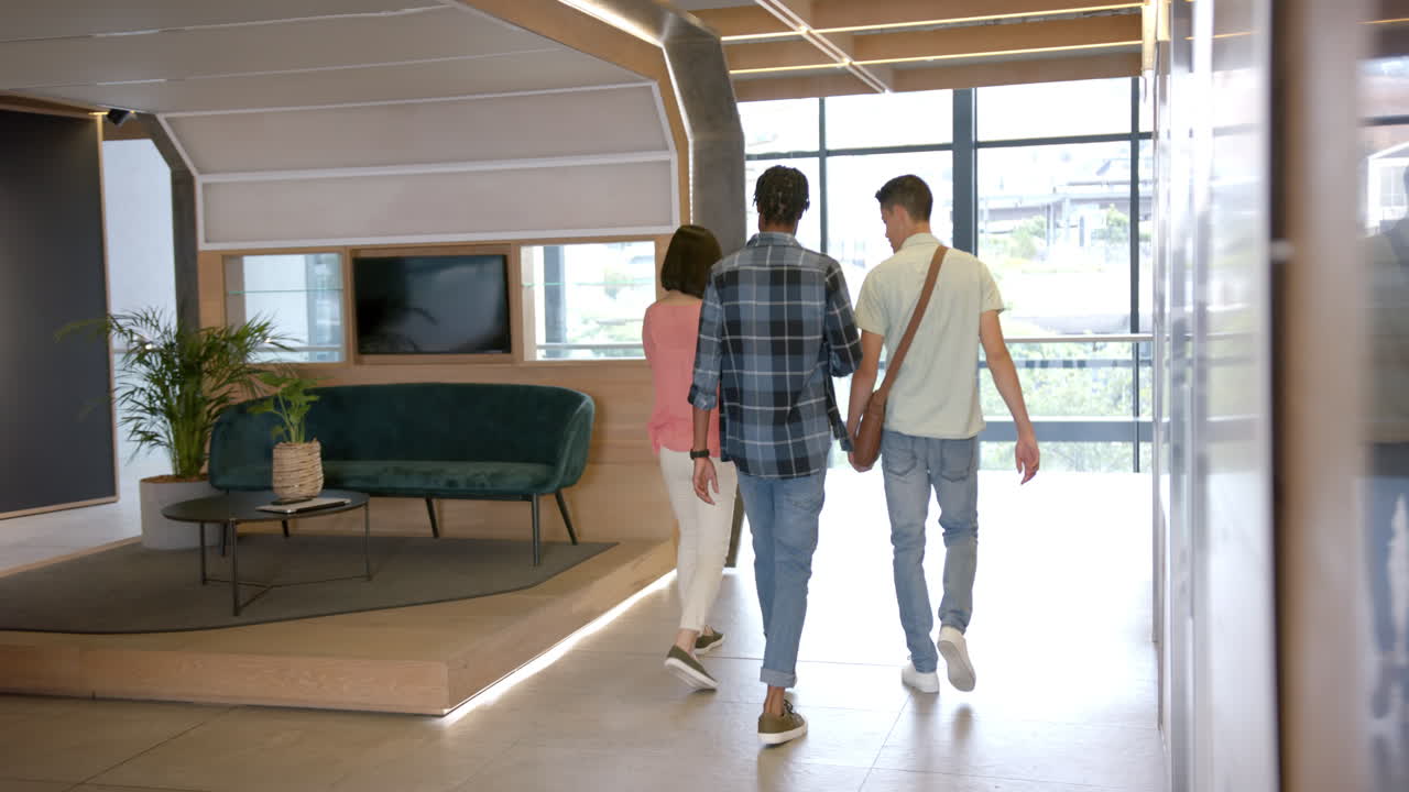 Walking together, three colleagues discussing work in modern office hallway