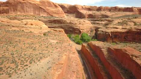 Rising-Aerial-View-Above-Train-Tracks-Cutting-Through-a-Canyon-in-the-Desert-Lands-of-Moab,-Utah