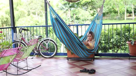 mujer navegando por el teléfono inteligente y descansando en la hamaca