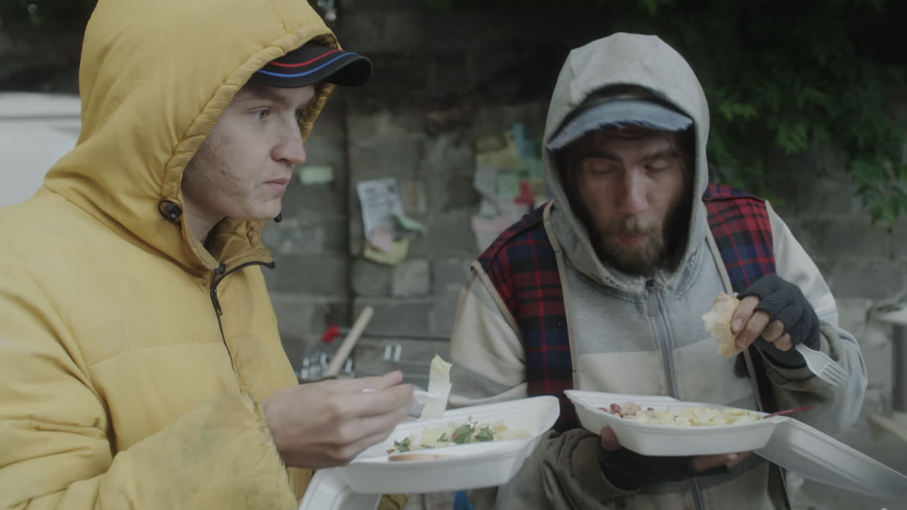 Homeless men eating food outdoors, likely from a charity service
