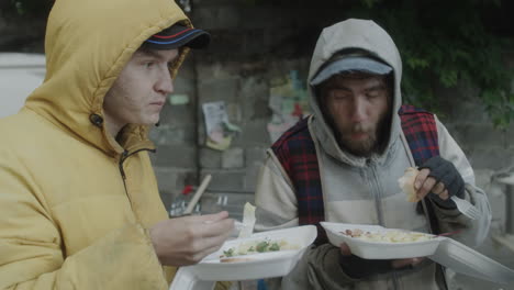 homeless men eating food outdoors, likely from a charity service