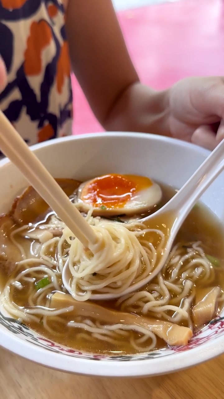 Una mano solleva spaghetti ramen con le bacchette sopra una ciotola, illuminazione naturale brillante, profondità di campo ridotta.