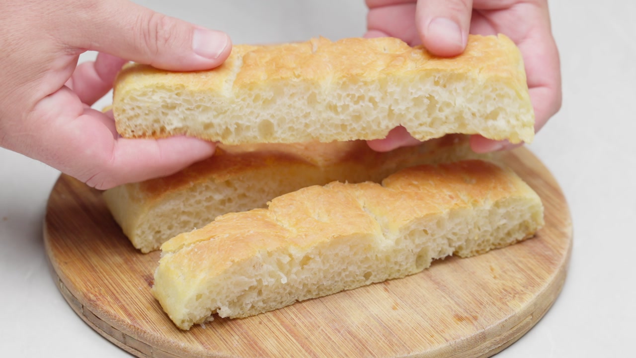 Close up of hands revealing soft focaccia crumb on wooden board