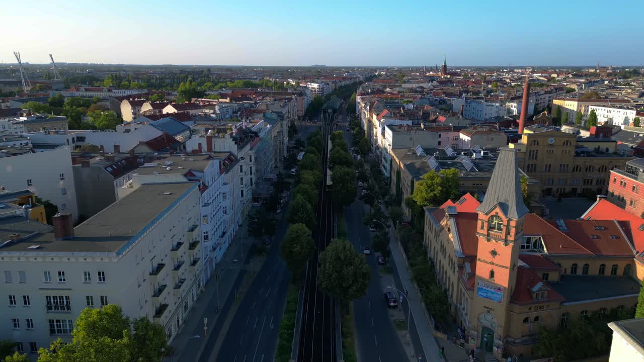 Žlutý nadzemní vlak projíždějící obytnou čtvrtí Berlína v létě. Velkolepý letecký záběr dronu s letem pozpátku.
