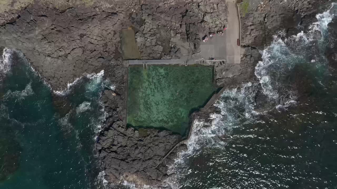 Drone top down rises above open ocean salt water natural pool on peninsula in Kiama NSW Australia