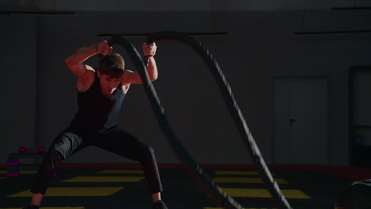 Uomo che esegue un intenso allenamento con le battle rope al rallentatore in palestra.
