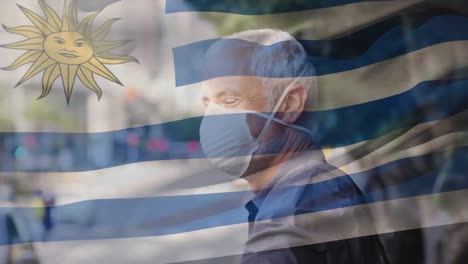 Animation-of-flag-of-uruguay-waving-over-caucasian-man-wearing-face-mask-in-city-street