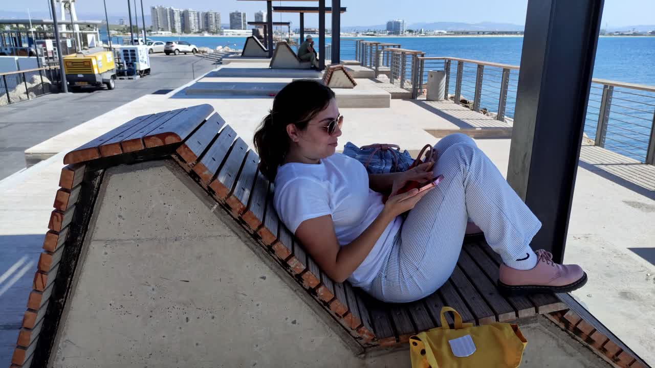 Side view of a tourist using smartphone on a deck by the sea