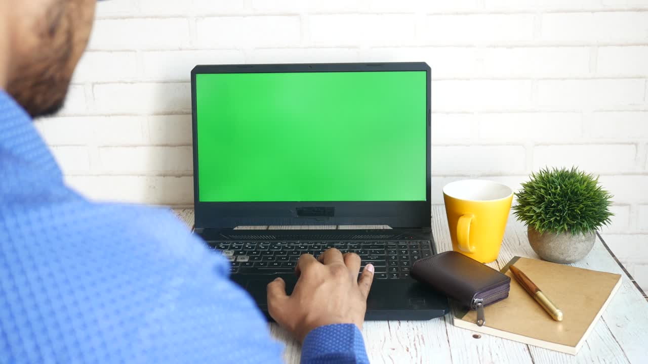 rear view of young man using laptop with blank screen on office desk.