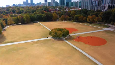 aerial drone shot slowly flying around a patch of trees at the center of the softball fields at piedmont park in downtown atlanta, georgia