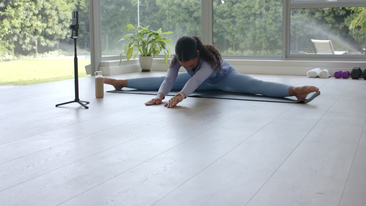 On raising head, woman is adjusting hands and rising into upright straddle on mat near window