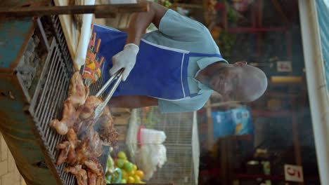 vertical view of a man grilling chicken at the marketplace in kampala, uganda, africa