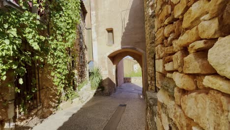 Kleine-Romantische-Alte-Gasse-In-Einem-Kleinen-Dorf-In-Frankreich-Mit-Alten-Steinmauern-Und-Vielen-Pflanzen-Und-Torbogen-Bei-Gutem-Wetter