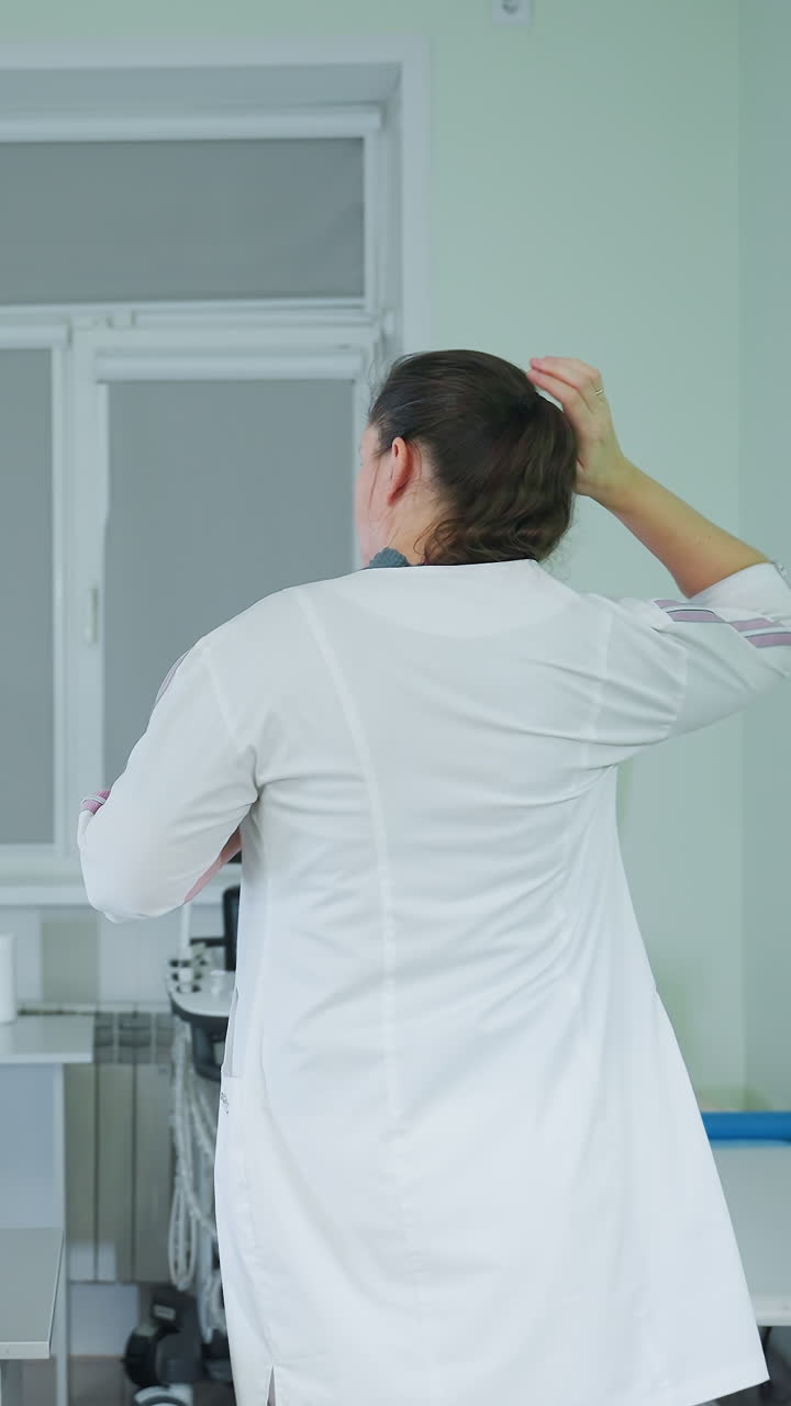 Técnica ecografista blanca preparando la bata y el equipo, revisando el monitor de ultrasonido, la estación de trabajo clínica, los cables y la sonda visibles, ajustes enfocados, análisis de datos, profesional tranquila