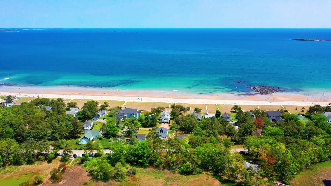 Scenic drone shot of Saco, Maine coastline packed with visitors. Sand, surf, and vacation homes buzzing with life. Atlantic Ocean waves make this East Coast beach a perfect summer tourist paradise.
