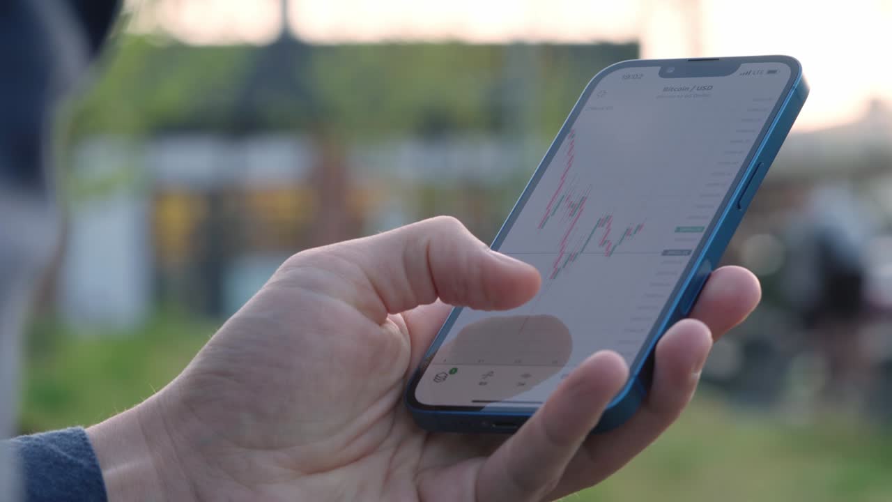 4k 남자는 스마트폰 화면에서 암호화폐 거래의 불 차트를보고 있습니다.