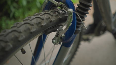 primer plano de alguien probando la funcionalidad del freno delantero de una bicicleta, el enfoque está en el neumático y el mecanismo del freno con un fondo borroso con marcas blancas