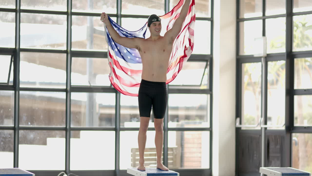 Male Swimmer holding American flag, standing on podium, celebrating victory indoors