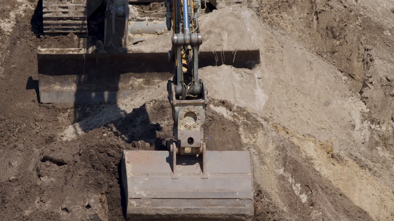 Excavator releases soil from bucket onto dirt slope, overhead view, bright daylight, steady camera