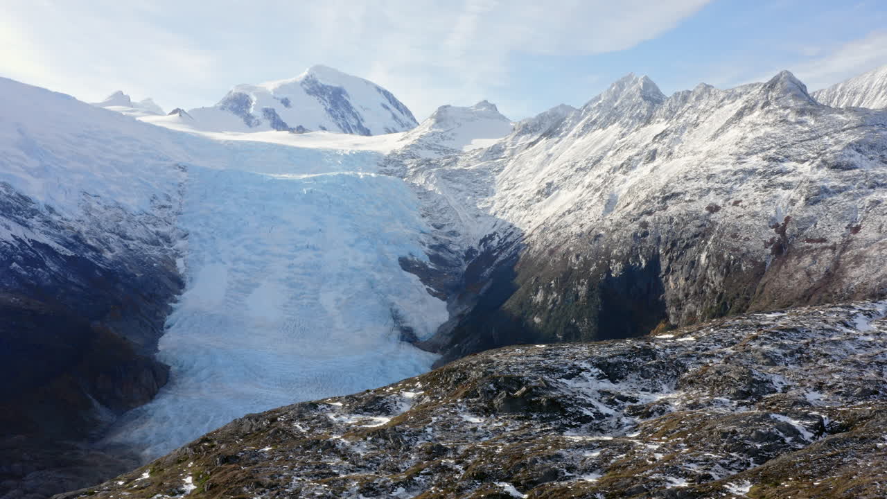 Massive glacier flows between mountain ridges under pale sky in frozen Cape Horn region, aerial tracking reveal left