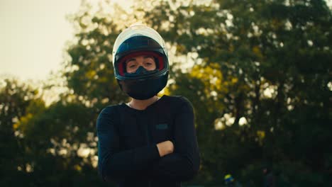 girl professionally motorcyclist posing in a black helmet and black clothes against the background of green trees