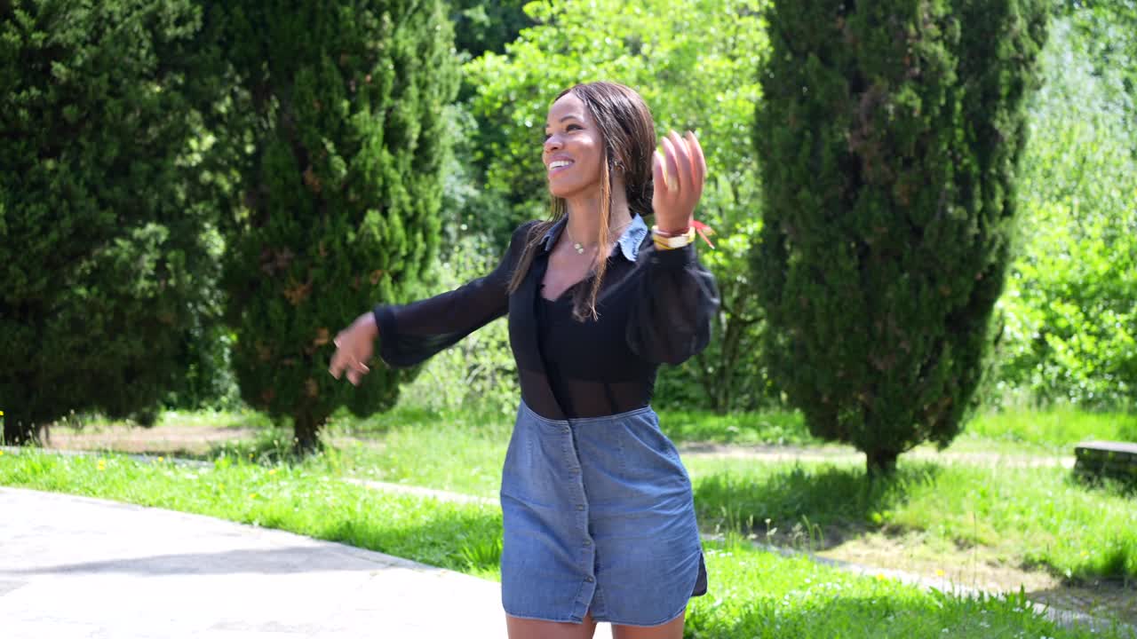 Woman in denim skirt and black blouse dancing outdoors