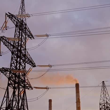 electricity pylon on industrial chimney background. high-voltage tower and pipe of power plant with smoke on evening sky. harmful smoke polluting the environment.