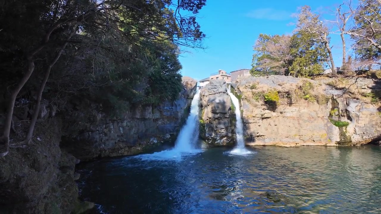Panorâmica suave mostrando a cachoeira caindo em uma piscina turquesa com margens rochosas
