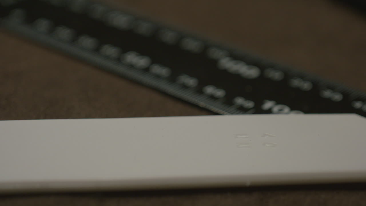 Detailed view of a white leather edge burnisher with embossed markings, placed beside a black measuring ruler on a brown surface.