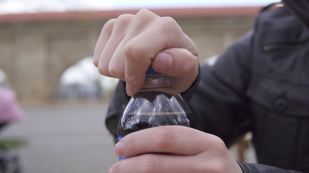 Closeup view of man's hands unscrewing the top from a soda bottle in the street cafe. Shot in 4k