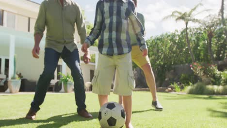 Glücklicher-Kaukasischer-Großvater-Mit-Erwachsenem-Sohn-Und-Enkel,-Der-Im-Garten-Fußball-Spielt