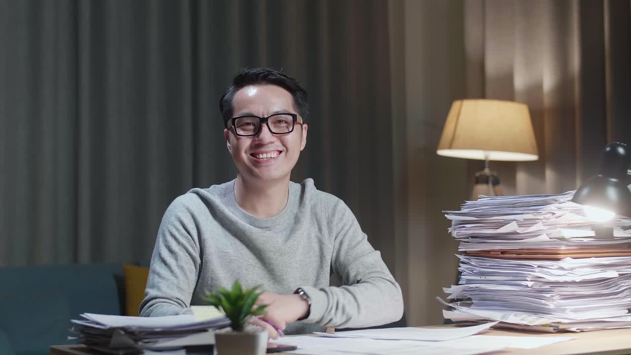 Asian Man Smiling To Camera While Working With Documents At Home