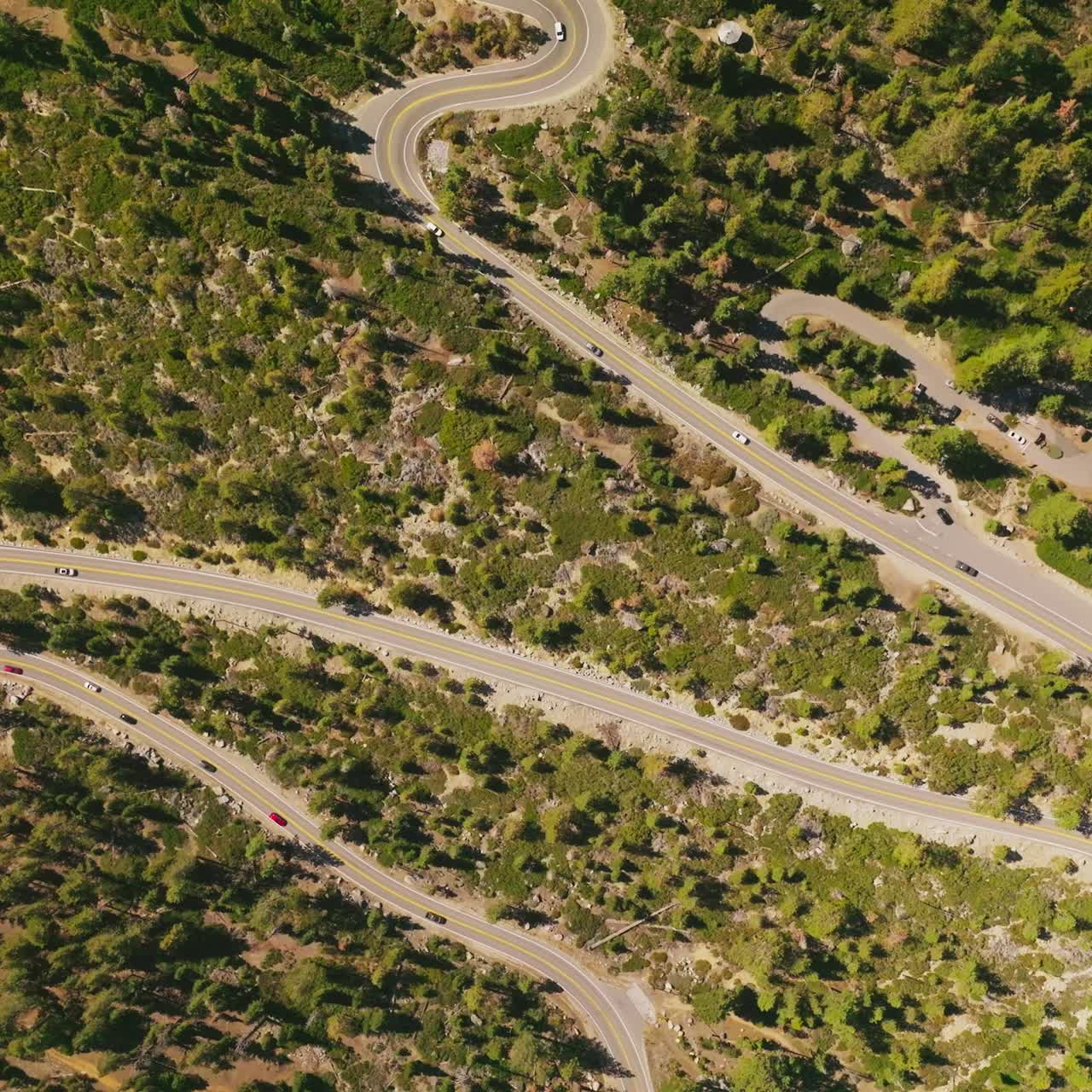 Cars moving leisurely by the winding road going through the green landscape. Drone descending over the highway on sunny daytime