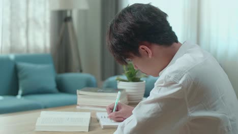 close up of asian man student writing in notebook on the table while studying at home