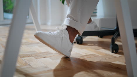 anónimo freelance sentado en un sillón de primer plano. zapatos blancos hombre se desliza hacia atrás silla