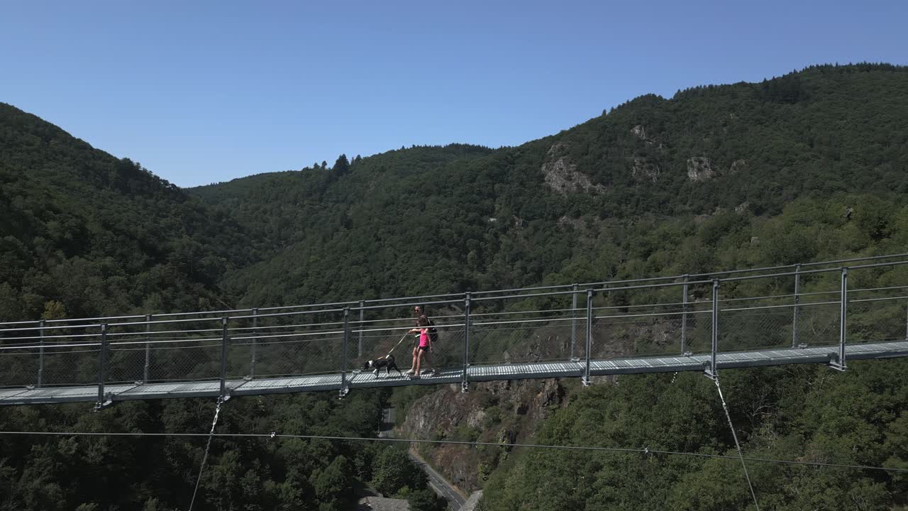 Una donna e una bambina portano a spasso il loro cane attraverso l'alta passerella di Mazamet. Questo panoramico ponte sospeso offre splendide viste estive sulla lussureggiante valle verde nella regione dell'Occitania.